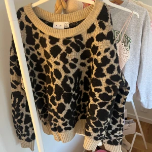 Leopardmönstrad stickad tröja från Vila - Säljer en beige och svart stickad tröja från Vila med leopardmönster. Tröjan har rund halsringning, ribbade muddar och lång ärm. Perfekt för dig som vill ha en cool och trendig look med djurmönster. Passar dig som gillar att sticka ut!