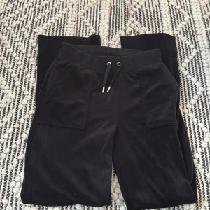 Svarta mjukisbyxor Juicy Couture XS - Svarta mjukisbyxor från Juicy Couture i mjuk sammet. Byxorna har snörning i midjan, stora fickor fram och bakfickor med knappar. Perfekta för en chill och avslappnad stil.