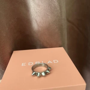 Silvrig ring med nitar från Edblad - Cool ring i silverfärgad metall från Edblad med flera spetsiga nitar på framsidan av ringen. Ringens storlek är 16.0