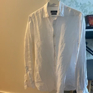 Vit linneskjorta från Massimo Dutti - Snygg och luftig vit skjorta i 100% linne från Massimo Dutti. Klassisk krage, långärmad och med knäppning framtill. Perfekt för en stilren och avslappnad look under varmare dagar. Storlek = S 