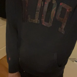 Mörkblå Polo Ralph Lauren hoodie - Säljer en mörkblå hoodie från Polo Ralph Lauren med stor broderad POLO-logga i färgglada mönster på bröstet. Tröjan har huva med snörning, magficka och långa ärmar. Perfekt för dig som gillar streetwear och klassisk stil.(personen är 185cm)Priset är justerbart