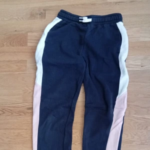 Mörkblå mjukisbyxor med färgblock - Mörkblå mjukisbyxor med vita och ljusrosa paneler längs sidorna. Byxorna har resår i midjan och snörning framtill för extra komfort. Perfekta för chill dagar eller träning. Mjukt material som känns skönt mot huden.