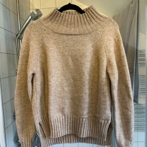 Beige stickad polotröja med slits S-M - Mysig beige stickad polotröja med bred ribbad krage och muddar. Tröjan har lång ärm och slitsar i sidorna nedtill för en chill och avslappnad vibe. Perfekt för lager-på-lager under kyliga dagar.