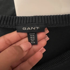 Mörkblå v-ringad tröja från GANT - Snygg mörkblå stickad tröja från GANT med v-ringning och diskret logga på bröstet. Tröjan har långa ärmar och ribbade muddar vid ärmslut och nederkant. Perfekt för dig som gillar klassisk och stilren look.