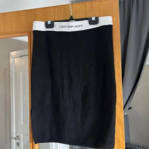 Svart stickad kjol Calvin Klein Jeans - Svart stickad kortkjol från Calvin Klein Jeans med vit elastisk midja där loggan är broderad. Enkel och clean design, tight passform och mjukt material som känns skönt mot huden. Perfekt för dig som gillar minimalistisk stil.