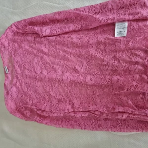 Rosa spetsblus med lång ärm - Säljer en superfin rosa blus i genombruten spets med lång ärm. Blusen har rund halsringning och är helt täckt av ett romantiskt spetsmönster som ger en cool och feminin vibe. Perfekt att styla lager på lager eller med ett linne under.