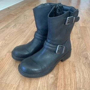Svarta boots med spännen och dragkedja - Snygga svarta boots i skinn med två silvriga spännen och dragkedja baktill. Insidan är fodrad med mjukt material för extra värme. Köpt för många år sen men använda max 3ggr då de tyvärr va för små redan från början. I princip inga tecken på användning. Väldigt mjuka och sköna på.