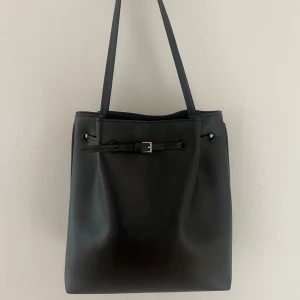 Rymlig väska med detalj - Svart axelväska i skinnimitation med en minimalistisk design! Endast använd några gånger i sommar och är i mycket gott skick 🤍