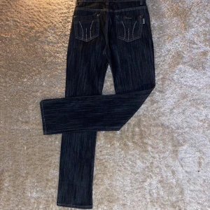 Mörkblå jeans med strassdetaljer - Snygga mörkblå jeans från Mumuk med raka ben och coola strassdetaljer på fickorna. Jeansen har kontrastsömmar och metallknappar med mönster. Passar dig som gillar att sticka ut med lite extra bling på dina jeans.