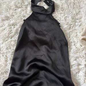 Svart halternecktopp från Zara - Snygg satin topp svart från Zara . Toppen har halterneck med bred krage och knäppning i nacken. Perfekt för dig som vill ha en stilren och elegant look med lite edge. Helt ny endast testad
