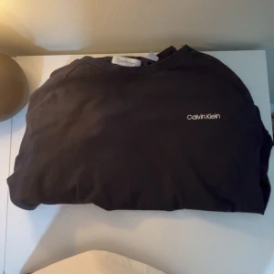 Svart sweatshirt från Calvin Klein - Säljer en svart sweatshirt från Calvin Klein med diskret broderad logga på bröstet. Tröjan har rund halsringning och är i mjukt bomullsmaterial. Perfekt för en stilren och enkel look.