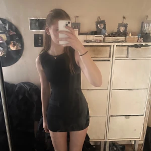 Svart kort klänning med bälte - Säljer en svart, ärmlös kort klänning med  matchande bälte. Enkel och stilren design som passar perfekt till olika tillfällen. Klänningen har rund halsringning och en figurnära passform. Den är även helt oanvänd pga för liten storlek, pris går att diskutera! 