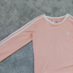 Rosa/peach adidas tröja - En oanvänd adidas tröja som är som ny. Ser dock att det är ett svart litet sträck på, men det går nog att tvätta bort.
