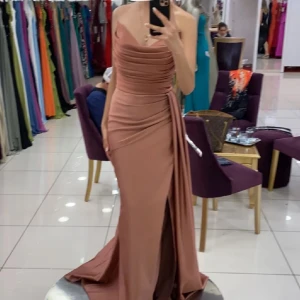 Rosa långklänning med drapering och slits - Säljer en elegant, axelbandslös långklänning i dammigt rosa med draperad överdel och markerad midja. Klänningen har en hög slits framtill, snörning i ryggen och ett vackert fall. Perfekt för bal eller fest. Endast använt en gång 🤍 Storlek Xs-S