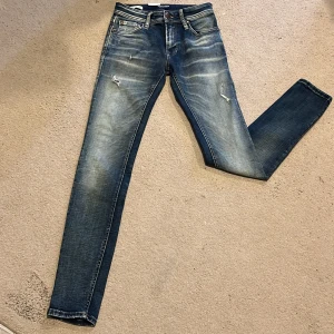 Blå skinny jeans från Jack & Jones - (Helt nya) Säljer ett par blå skinny fit jeans från Jack & Jones, modell Liam. Jeansen har slitna detaljer och klassisk femficksdesign. Perfekta för dig som gillar en tajt passform och en trendig, lite ruff look. 27/l32