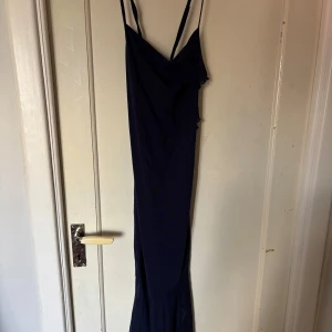 Mörkblå klänning  - Säljer en mörkblå långklänning med smala korsade axelband. Klänningen har en figurnära passform och volangdetalj framtill. 