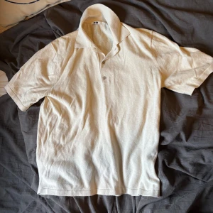 Beige pikétröja från Uniqlo - Säljer en stilren beige pikétröja från Uniqlo. Tröjan har korta ärmar, klassisk krage och knäppning med tre knappar framtill. Tillverkad i mjukt bomullsmaterial som känns skönt mot huden. Perfekt för en avslappnad och snygg look.