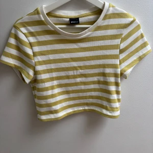 Grön och vit randig croppad t-shirt från Ginatricot - Säljer en croppad t-shirt från Ginatricot med vita och vita  ränder. T-shirten har korta ärmar och rund halsringning. Perfekt för varma dagar och enkel att matcha med jeans eller kjol!