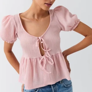 Ljusrosa blus med puffärm och knyt - Supersöt ljusrosa blus med puffärmar och två knyt framtill. Blusen har en lätt rynkad struktur! Jättefin sommartopp men kommer aldrig till användning. Nypris 279kr! (tröjan har en jätteliten fläck som man ser på 2a bilden) OBS! Jag har sytt igenom i mellan hålet för tyckte toppen var väldigt öppen! Det ser man också mellan knutarna. Skriv för frågor 💞