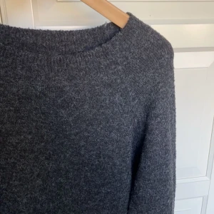 Mörkgrå stickad tröja från Vero Moda - Mysig mörkgrå stickad tröja från Vero Moda med rund halsringning och långa ärmar. Perfekt för kyliga dagar och enkel att matcha med olika outfits. Klassisk och tidlös modell som passar till det mesta.