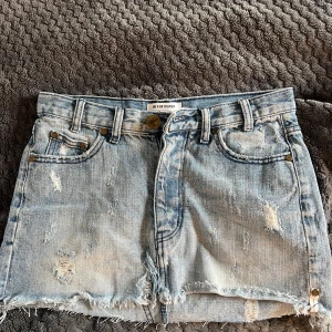 Ljusblå jeanskjol från One Teaspoon - Säljer en ljusblå jeanskjol från One Teaspoon med slitna detaljer och slitsning nertill. Den är lågmidjad och kort i modellen