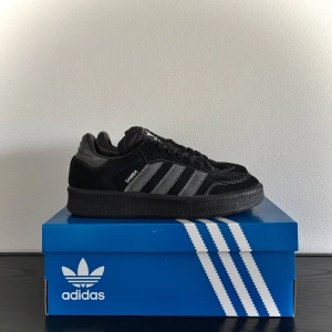 Adidas Samba OG svart/grå sneakers - Säljer ett par Adidas Samba OG sneakers i svart mocka med gråa detaljer och klassiska tre ränder på sidan. Skorna har svart sula, snörning och vit Adidas-logga på plösen. Perfekta för dig som gillar stilrena och tidlösa sneakers.  Sprayade skydd för smuts så kan ej lämna tillbaka. Köpte för 1450kr. 