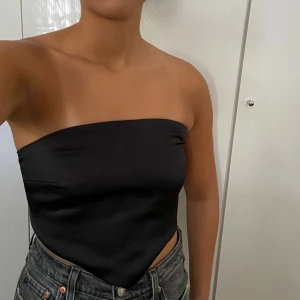 Tubtopp svart - Fin festtop i glansigt material, stretch där bak. Litet hål i mitten på sidan, går nog lätt att sy igen.