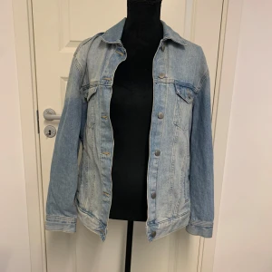 Ljusblå jeansjacka - Klassisk ljusblå jeansjacka med knappar framtill och två bröstfickor med lock. Jackan har långa ärmar och raka sömmar, perfekt för en avslappnad stil. Passar dig som gillar tidlös denim och enkel design.