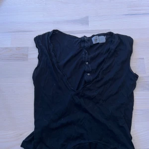 Svart ärmlös topp från Velour - Svart ärmlös topp från Velour med v-ringning och knappar baktill. Perfekt för en stilren och enkel look. Mjukt material som känns skönt mot huden.