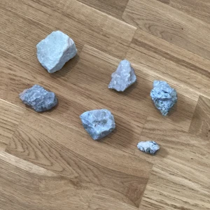 Samling av råa mineralstenar - Säljer en samling med sex råa mineralstenar i olika storlekar och former. Stenarna har en ljusblå till grå färg och är oregelbundet formade. Perfekt för dig som gillar kristaller eller vill dekorera med naturliga mineraler.