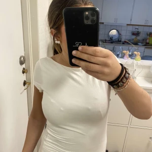 Vit topp med draperad rygg från Gina Tricot - Säljer en vit topp från Gina Tricot med korta ärmar och snyggt draperad, djup rygg. Toppen är i mjuk bomull och har en tight passform. Perfekt att styla till jeans eller kjol för en clean look.