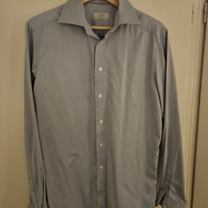 Ljusblå skjorta från Eton - Säljer en ljusblå skjorta från Eton. Skjortan har lång ärm, klassisk krage och knappar framtill. Tillverkad i 100% bomull med ett diskret mönster som ger en stilren look. Perfekt för dig som gillar klassisk stil.