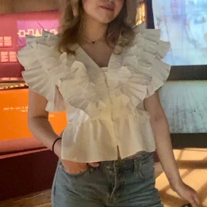 Vit volangblus  - Säljer en vit blus med stora volanger längs axlar och bröst, samt v-ringning. Blusen har korta ärmar och knäppning framtill. 💘💘💘