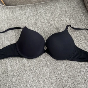 Svart push-up bh från Dorina - Säljer en svart push-up bh från Dorina med släta kupor och justerbara axelband. Bh:n har en klassisk design och är tillverkad i mjukt syntetmaterial för en bekväm känsla hela dagen.