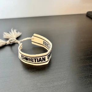 Christian Dior J'Adior armband - Snyggt armband från Christian Dior i beige och svart med texten 'CHRISTIAN DIOR J'ADIOR'. En perfekt liten detalj i din outfit. Hör av er vid frågor! 