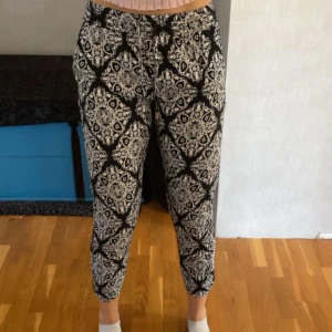 Svartvita mönstrade byxor från Amisu - Snygga svartvita byxor från Amisu (New Yorker) i storlek 34. Byxorna har ett unikt, blommigt mönster, med snörning och resår i midjan. De är väldigt mjuka och luftiga vilket gör den sköna på varma sommardagar. Tyvärr är det ett litet hål på utsidan av ena benet men det går väldigt lätt att sy igen! Räcker med några stygn☺️