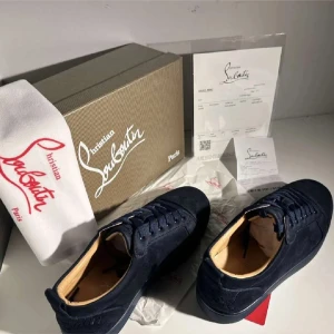 Mörkblå sneakers från Christian Louboutin - Snygga mörkblå sneakers från Christian Louboutin i mocka med ton-i-ton broderad logga på hälen. Skorna har rund tå, platt sula och klassisk snörning. Insidan är fodrad i ljust skinn för extra komfort. Perfekta för dig som gillar exklusiv streetstyle.