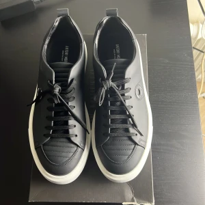 Svarta sneakers från Antony Morato - Stilrena svarta sneakers från Antony Morato med vit platt sula och snygga detaljer. Skorna är i skinn och har snörning framtill samt diskret logga på sidan. Perfekta för dig som gillar en clean och modern look. Rikdigt snygga skor men är inte storlek 43 för dom är för stora för mig skulle säga att dom är 44. Aldrig använt dom men ger ett bra pris på dom och lådan kommer också. Orginalpris 1895kr 