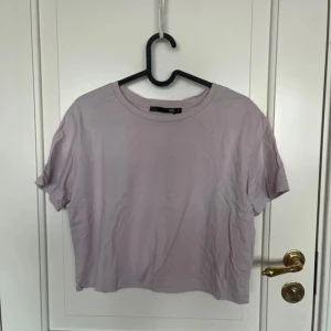 Ljuslila t-shirt från 157, storlek S - En basic ljuslila t-shirt från 157 i storlek S. Modellen är croppad med korta ärmar och rund halsringning. Tillverkad i mjuk bomull som känns skön mot huden. Perfekt till jeans eller shorts för en chill look.