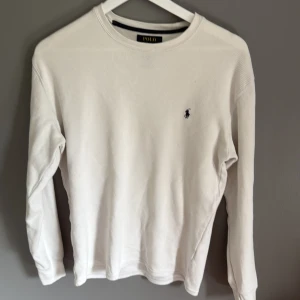 Vit långärmad tröja från Polo Ralph Lauren - Klassisk vit långärmad tröja från Polo Ralph Lauren med rund halsringning och den ikoniska broderade loggan på bröstet. Tröjan är i mjuk bomull och har en clean, stilren look som passar perfekt till jeans eller chinos.