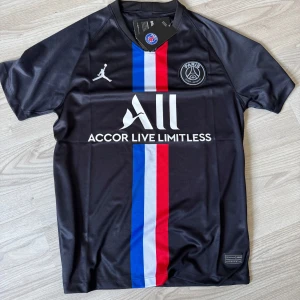 PSG svart matchtröja Jordan x Nike - Svart PSG fotbollströja med Jordan-logga och klubbmärke på bröstet. Snyggt vertikalt rött, vitt och blått band i mitten. Kortärmad modell i lätt och ventilerande material, perfekt för träning eller match.