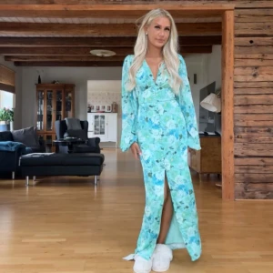 Blommig långklänning i blått och grönt - Superfin långklänning från adoore med blommigt mönster i blåa och gröna toner. Klänningen har v-ringning, långa ärmar och en snygg slits framtill. Knappar längs bröstet och lätt figursydd passform. Använd endast 1 gång.