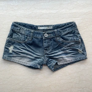 Jätte Lågmidjade shorts - Snygga blå jeansshorts från Fashion Jeans med slitna detaljer och klassisk femficksdesign. Shortsen har låg midja, ljusa tvättade partier och råa kanter för en cool look. Perfekta för varma dagar när du vill ha en avslappnad stil.