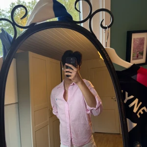 Rosa linneskjorta från Polo Ralph Lauren - Säljer en klassisk rosa skjorta från Polo Ralph Lauren med blå broderad logga på bröstet. Skjortan har lång ärm, knappar framtill och är gjord i luftig bomull. Perfekt för en clean och fräsch look. Krympt som fan i tvätten, egentligen M men passar bara S