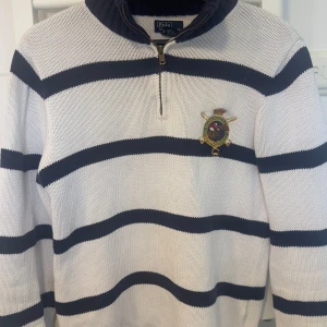 Randig Polo Ralph Lauren  - Snygg stickad tröja från Polo Ralph Lauren i vitt och mörkblått med breda ränder. Halv dragkedja vid halsen och broderad patch med polospelare på bröstet. Klassisk och sportig vibe, perfekt till jeans eller chinos. Passar mig som är 187cm