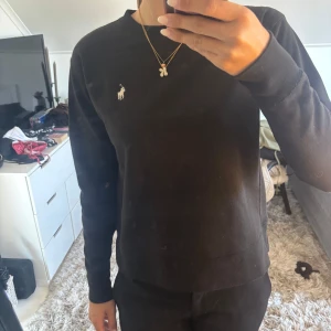 Svart tröja från Polo Ralph Lauren XS - Svart långärmad tröja från Polo Ralph Lauren i klassisk modell med rund hals och broderad logga på bröstet. Tröjan är i mjuk bomull och har en clean, stilren look som passar till allt. Perfekt för dig som gillar enkel och tidlös stil.