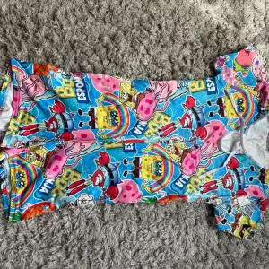 Färgglad Spongebob kortklänning - Superrolig kortklänning med Spongebob-tryck i blått, rosa, gult och rött. Klänningen har korta ärmar och är täckt av karaktärer från Spongebob Squarepants. Perfekt för dig som älskar färg och tecknade motiv! Materialet känns mjukt och stretchigt.