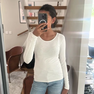 Vit långärmad topp i bomull - Säljer en enkel och fräsch vit långärmad topp i mjuk bomull. Modellen är figurnära med rund halsringning och passar perfekt till jeans eller kjol. Stilren och lätt att matcha med andra plagg.