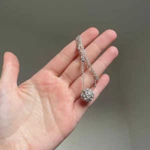 Glittrigt halsband med silverkedja - Snyggt halsband med tunn silverfärgad kedja och en rund, glittrig pärla täckt av små kristaller. Perfekt statement-piece för dig som gillar att sticka ut med lite extra bling. Justerbar längd på kedjan för att passa din stil.