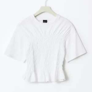 Vit smockad topp från Gina Tricot - Supersöt vit topp från Gina Tricot med smockad midja och lätt volang nertill. T-shirttyp med korta ärmar och rund halsringning. Perfekt för dig som gillar en feminin och trendig look. Gjord i mjuk bomull som känns skön mot huden.